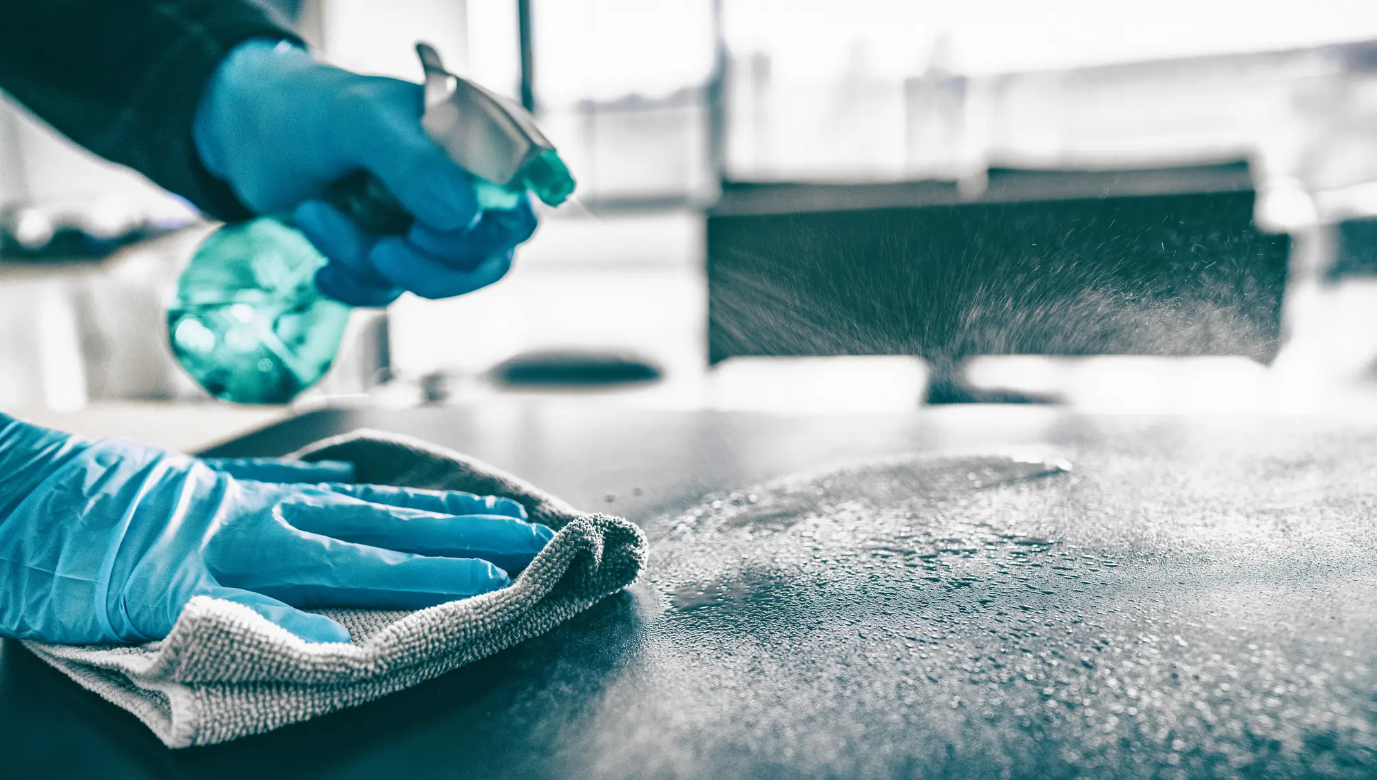 Eine Person mit blauen Handschuhen reinigt eine dunkle Oberfläche mit Spray und Tuch