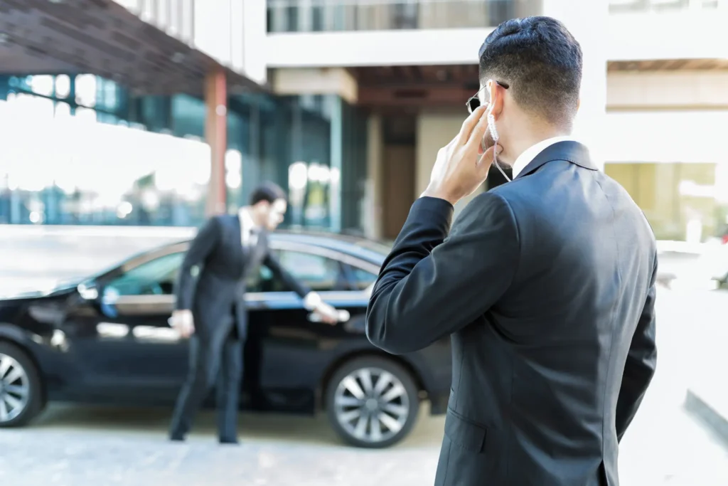Ein Mann im dunklen Anzug telefoniert, während ein anderer das Auto öffnet