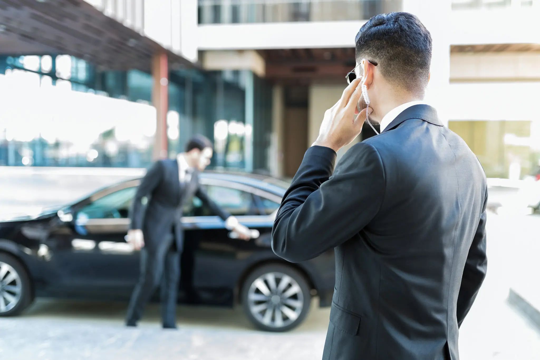 Ein Mann im dunklen Anzug telefoniert, während ein anderer das Auto öffnet
